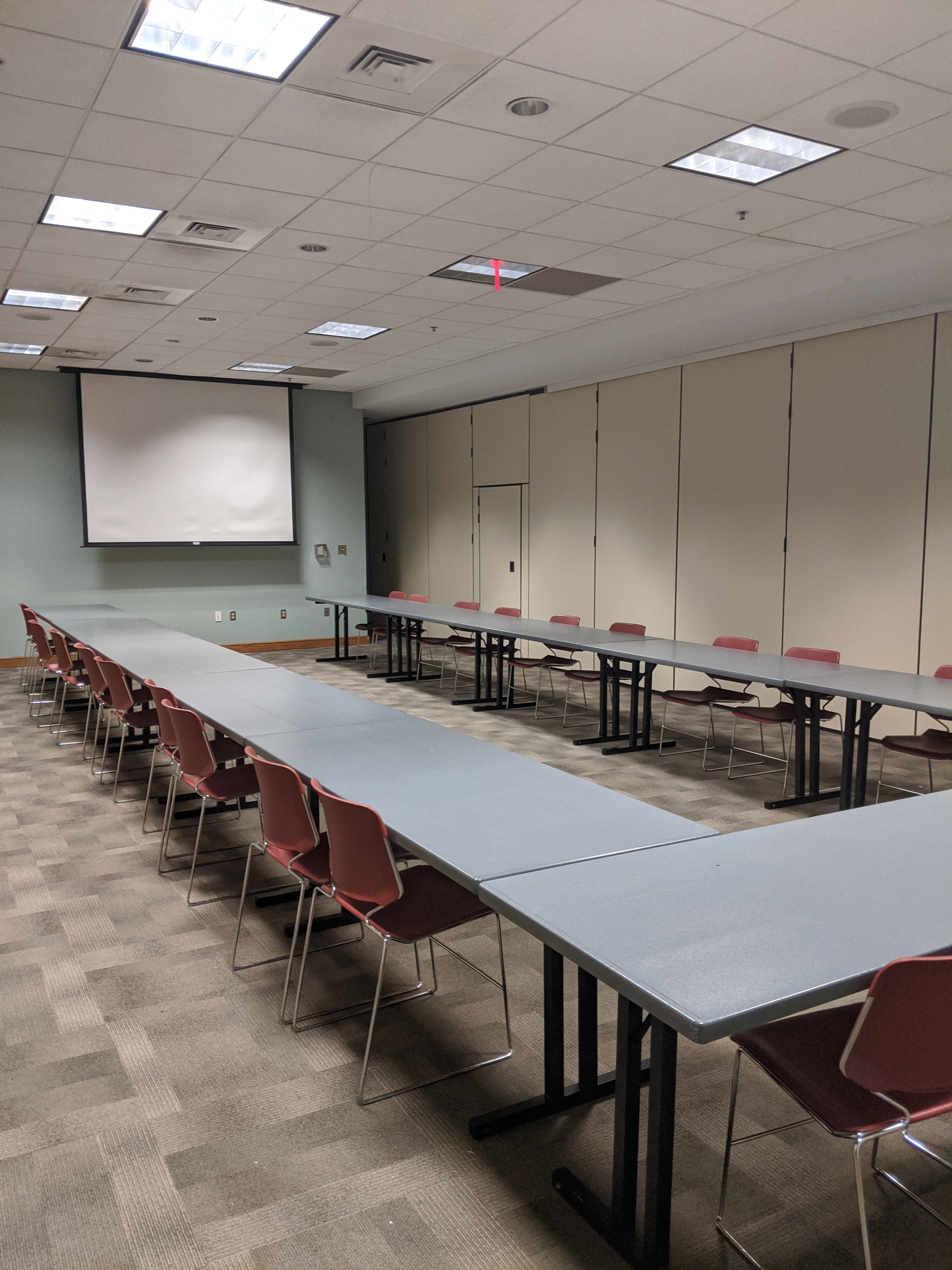 Photo of Multipurpose Room A with tables arranged in a U-shape facing  projector screen