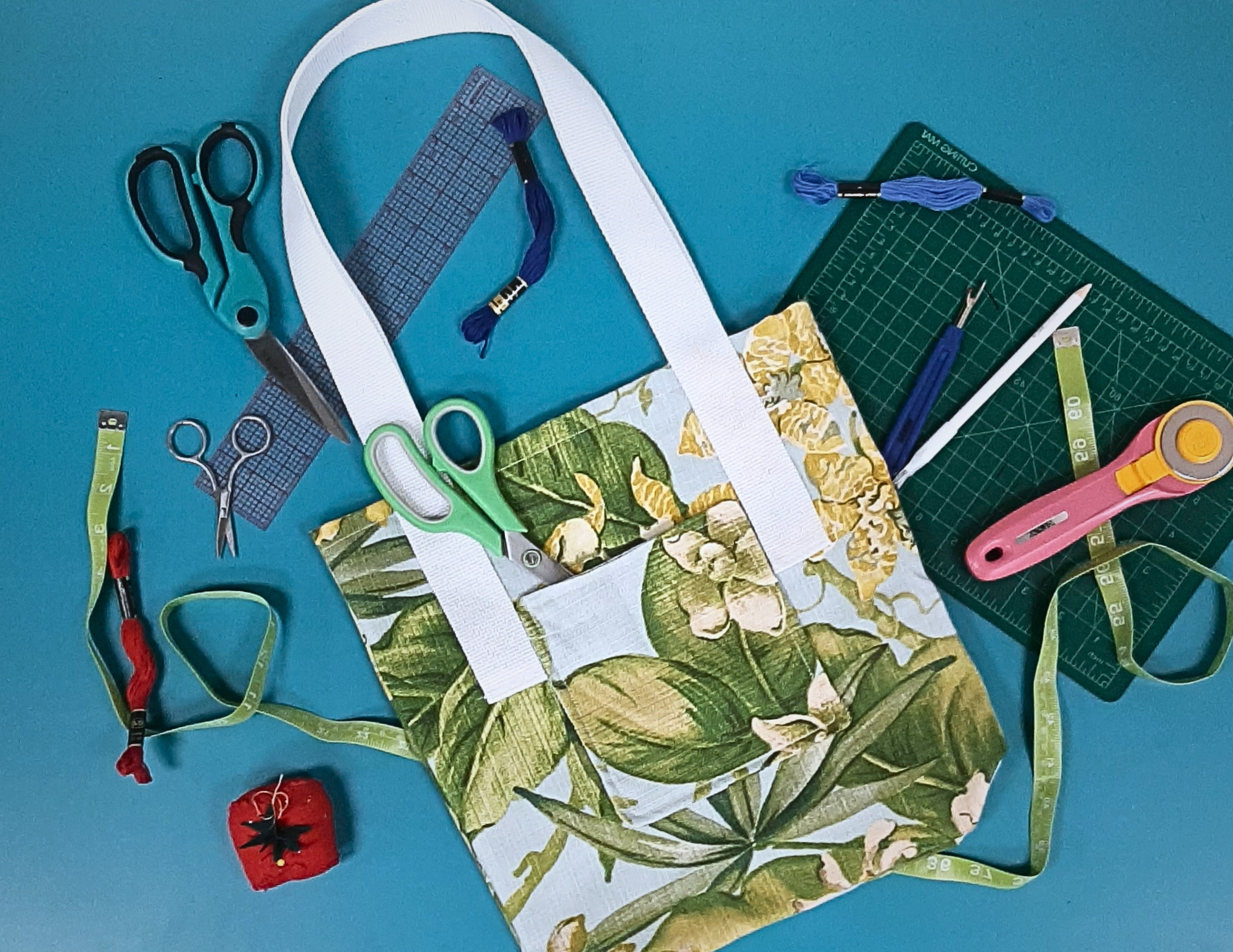 tropical patterned tote bag with white handles surrounded by sewing supplies. 