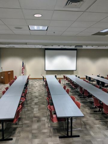 Room photo of Multipurpose Room BC showing tables in long parallel rows with projector screen pulled down