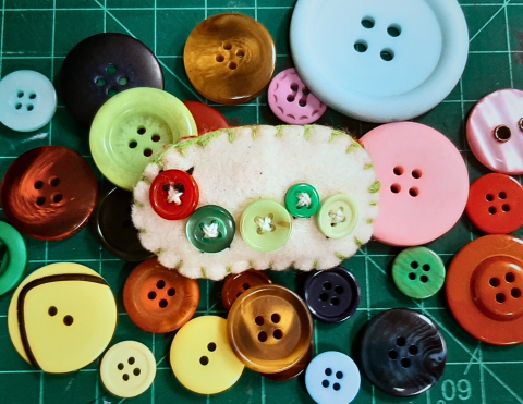 a felt brooch featuring a caterpillar made out of buttons 