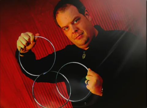 Photo of Chris Campbell holding three magic rings on a red background 